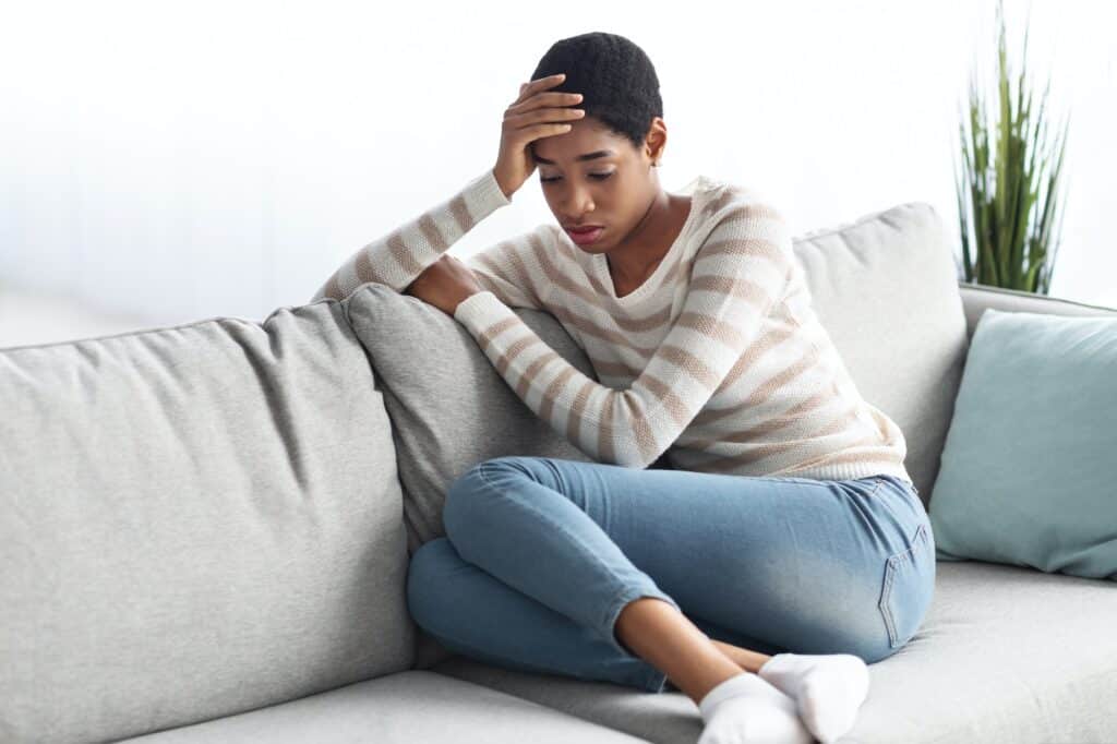 Seasonal Depression. Portrait Of Sad Black Female Sitting On Sofa At Home